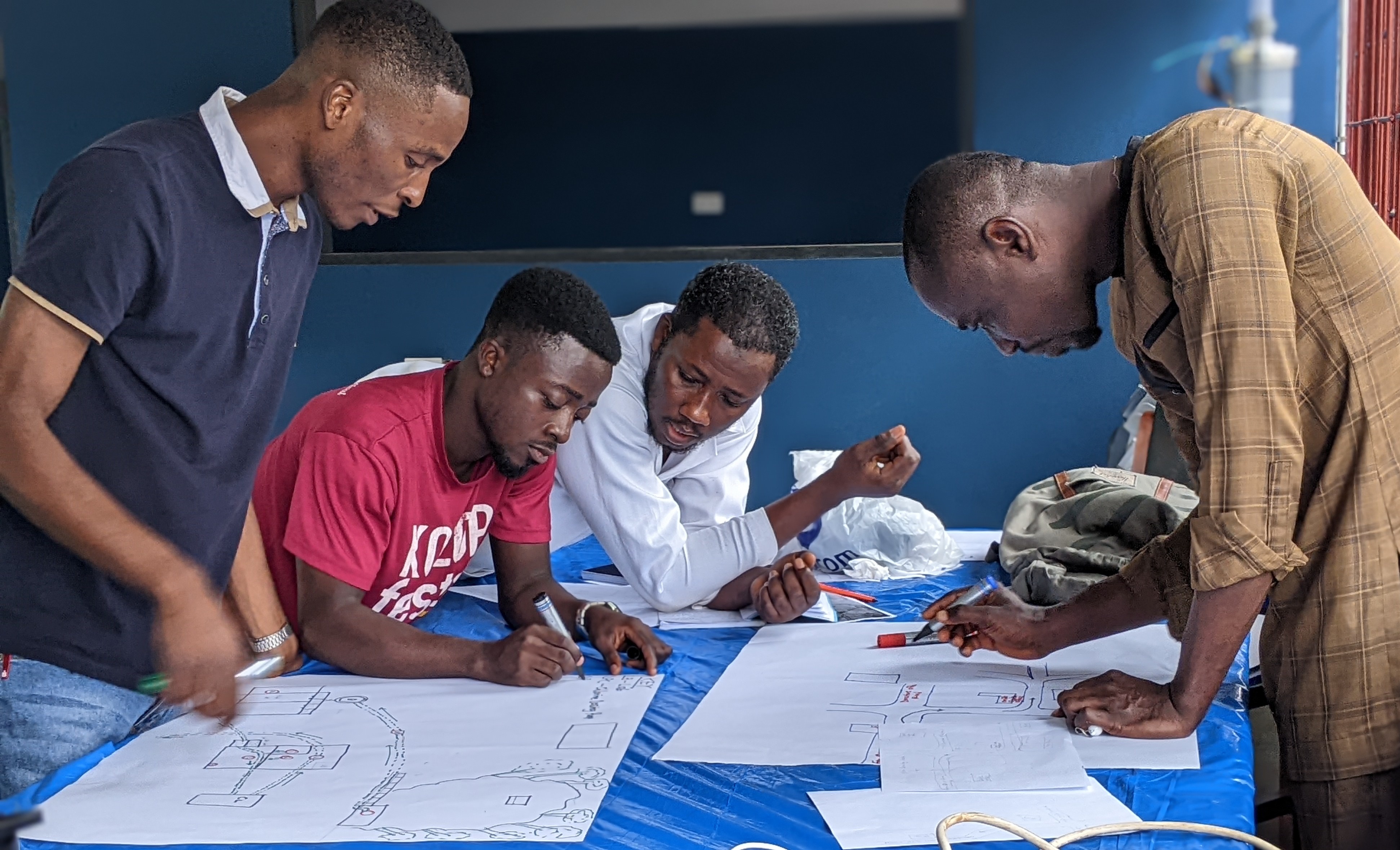 Four men collaborating in a hands-on learning activity, focused on their work at a table covered with a blue tarp in a training setting